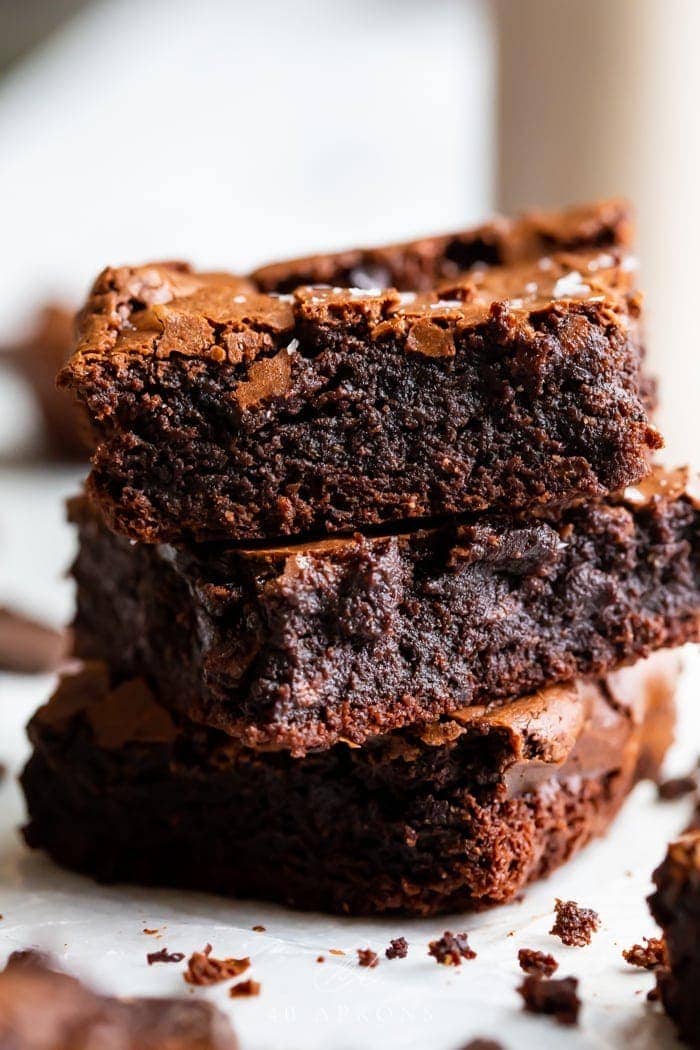A stack of three paleo brownies showing how fudgy and rich they are, with a crackly top and flake sea salt on top