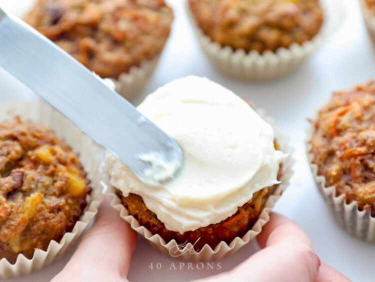 Cream cheese frosting being spread onto the top of a carrot cake cupcake.