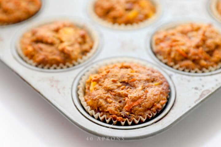 Baked, unfrosted carrot cake cupcakes in a silver metal muffin pan.