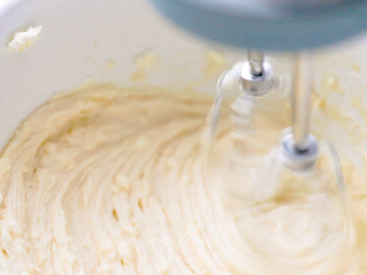A hand mixer beats together a cream cheese cupcake frosting until it's smooth and fluffy.