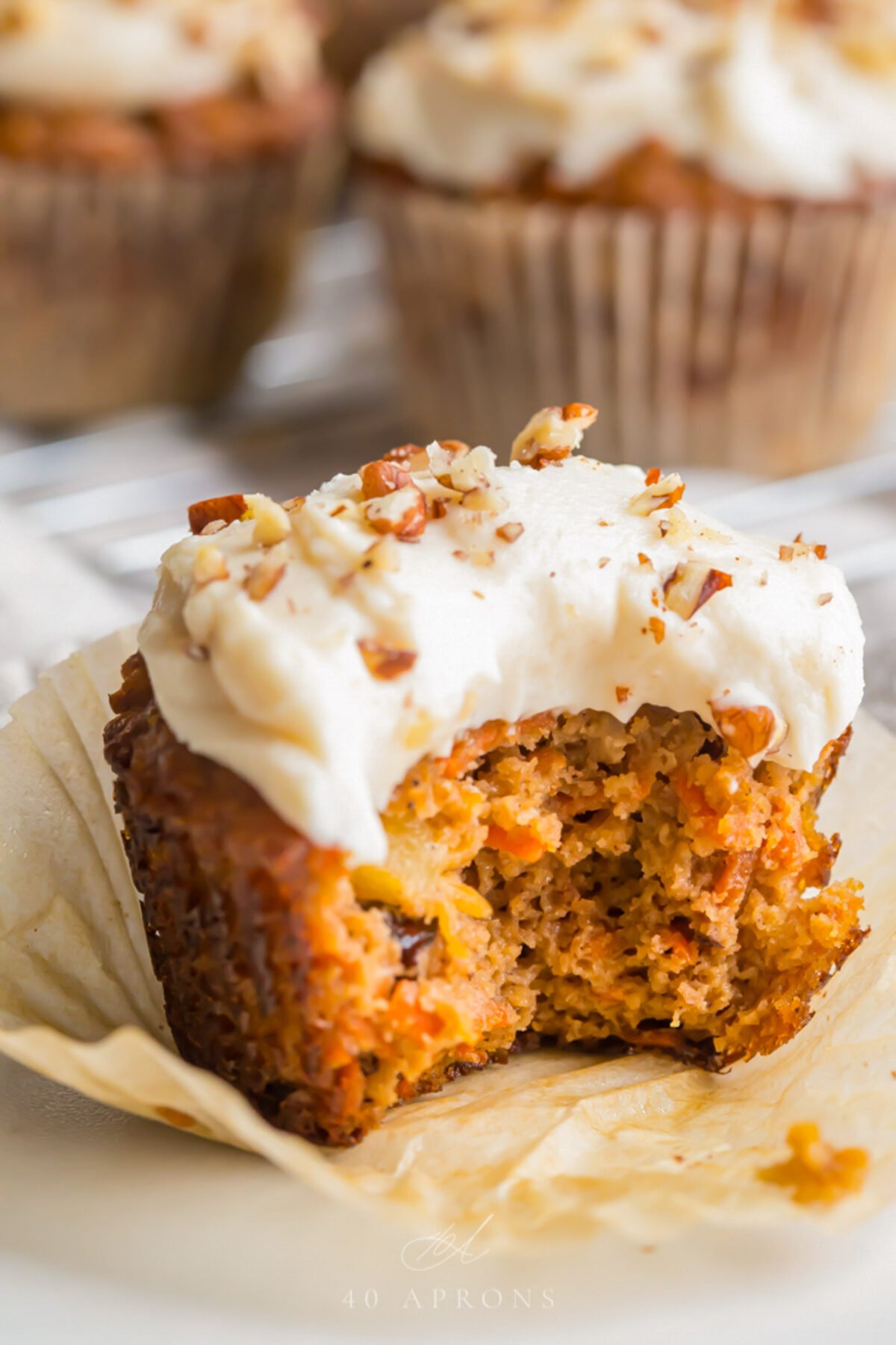 A paleo carrot cake cupcake topped with cream cheese frosting and chopped pecans. A bite is missing from the cupcake.