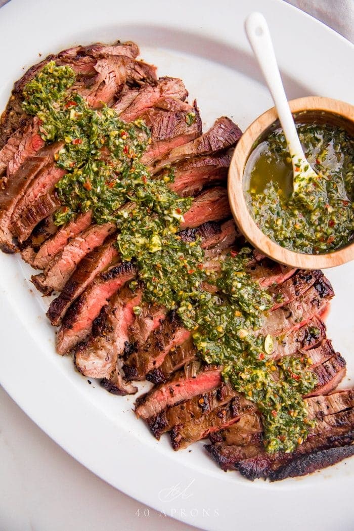 Sliced medium rare flank steak on a plate with lots of fresh chimichurri sauce on top