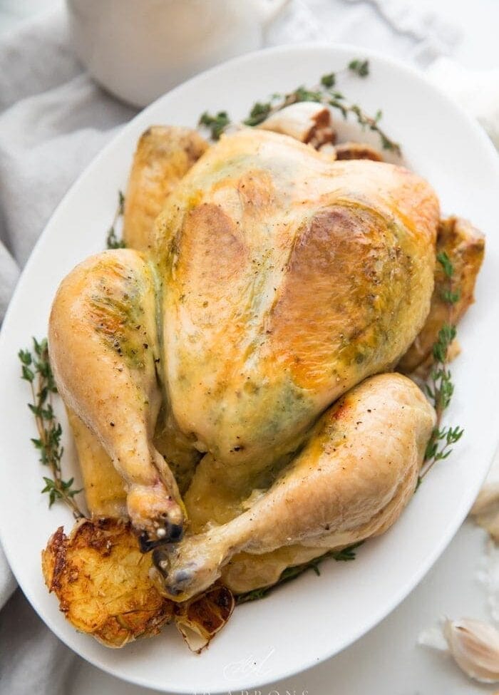 A slow cooker whole chicken with herb garlic butter visible under the skin on a plate with herbs and garlic
