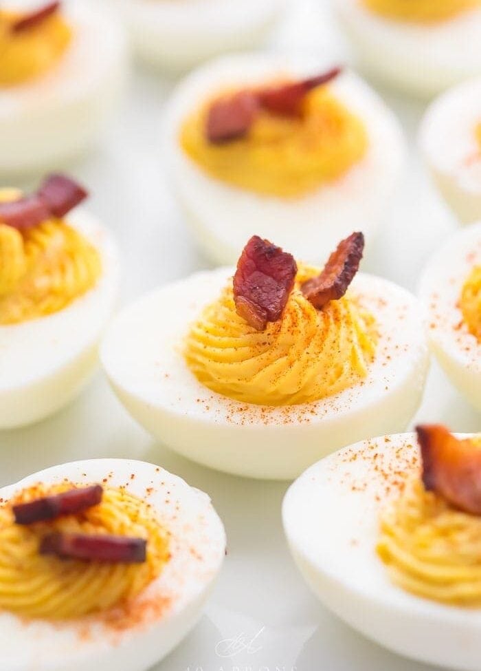 Deviled egg with a couple pieces of bacon on top surrounded by other eggs