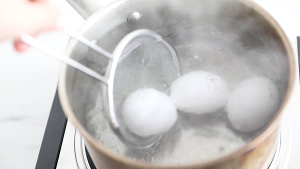 A handheld strainer lowering eggs into hot water