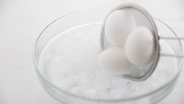 Strainer putting boiled eggs into a water bath