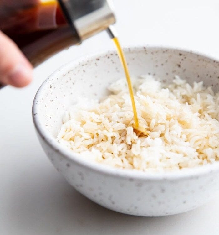 A bottle of soy sauce substitute pouring over a bowl of white rice