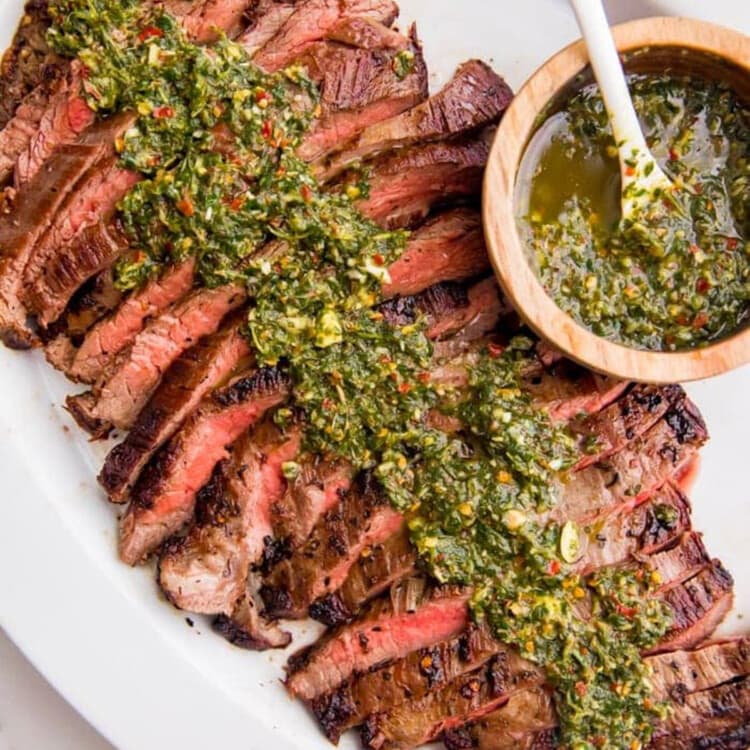 Overhead view of a platter of sliced flank steak coated in chimichurri.