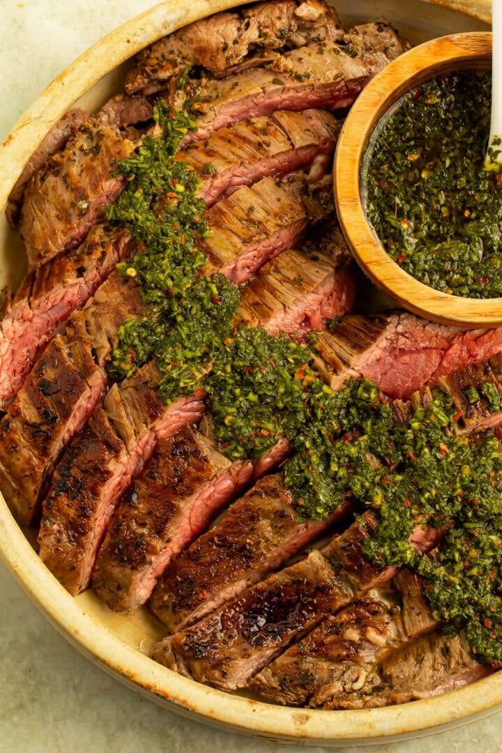 Close up of a dish of sliced flank steak topped with chimichurri sauce.