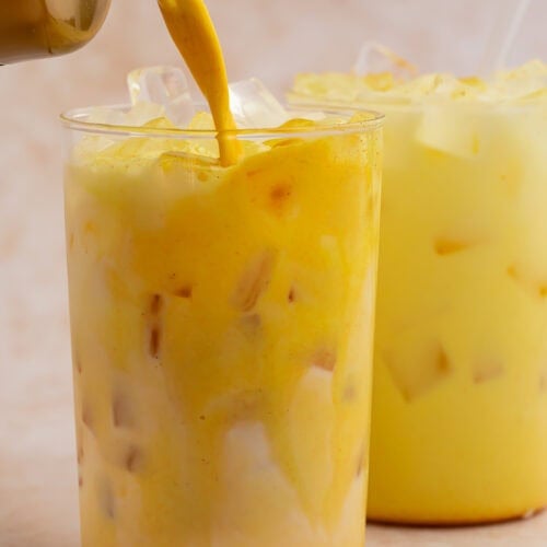 Iced golden milk latte being poured into a glass filled with ice.