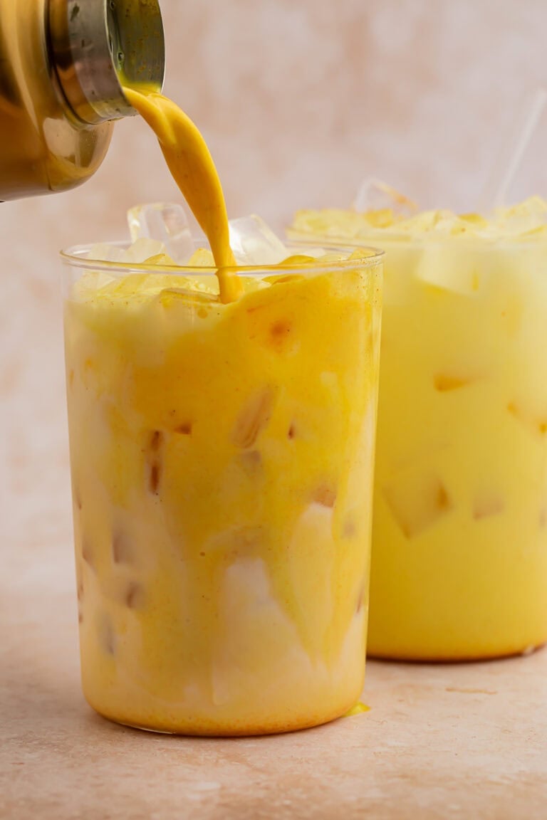 Iced golden milk latte being poured into a glass filled with ice.