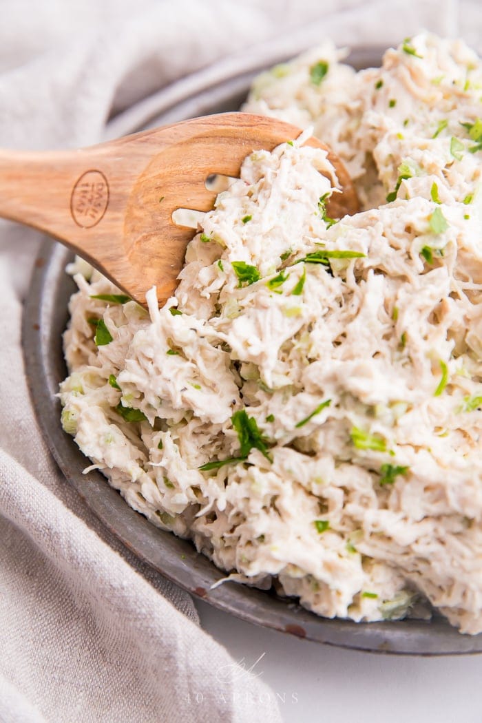 A bowl of shredded chicken salad with wooden spoon in