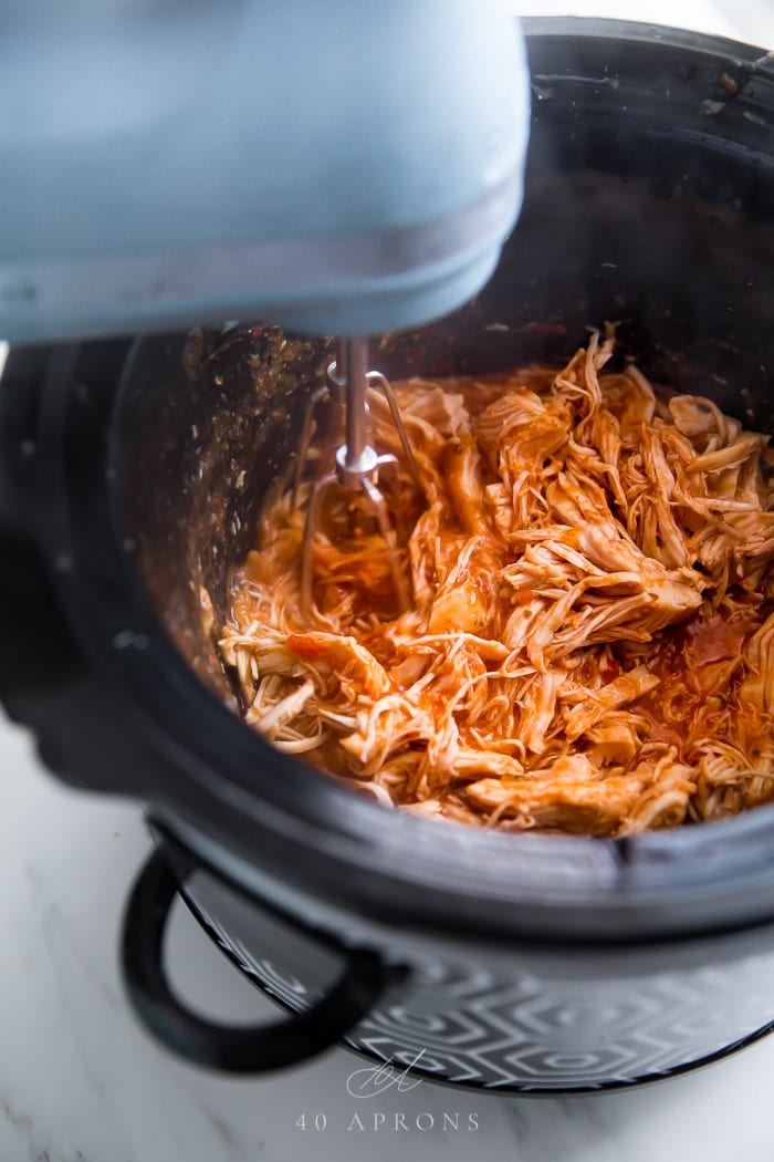 A hand mixer shredding chicken breasts in the slow cooker