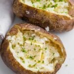 Baked potatoes from the grill on a plate open with pats of butter and chives