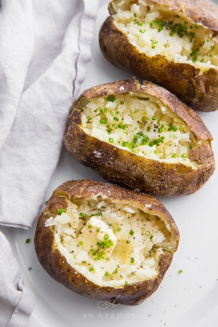 A row of baked potatoes from the grill open on a white plate with butter
