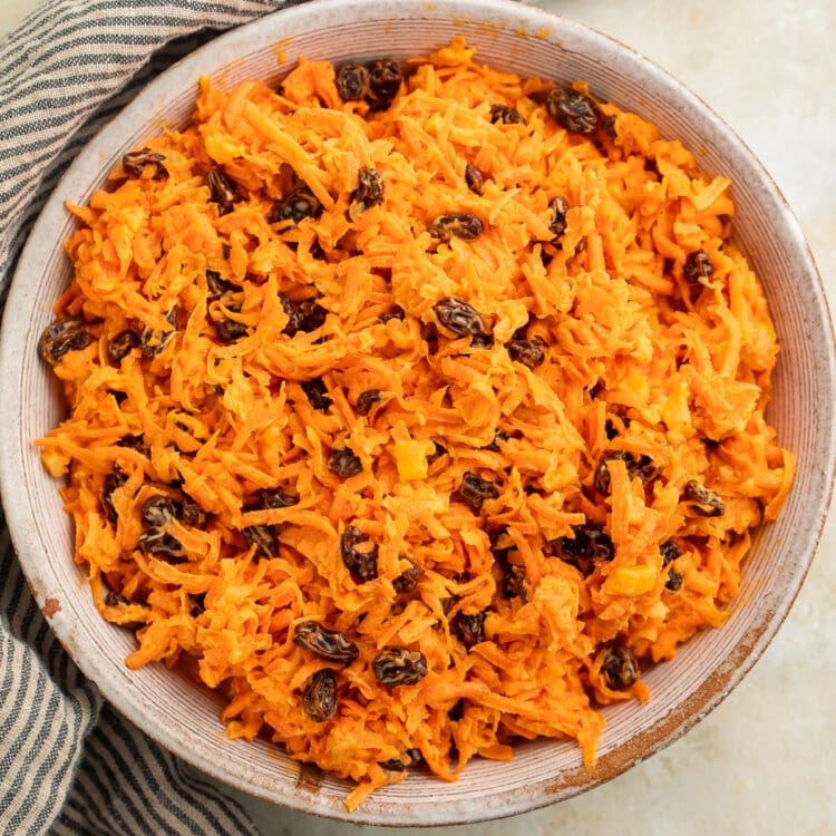 Overhead view of a bowl of carrot raisin salad on a table with a striped napkin.