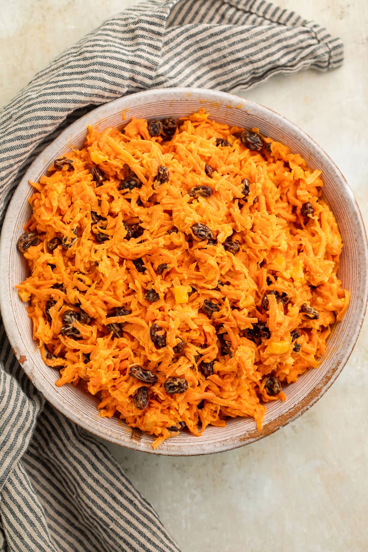 Overhead view of a bowl of carrot raisin salad on a table with a striped napkin.