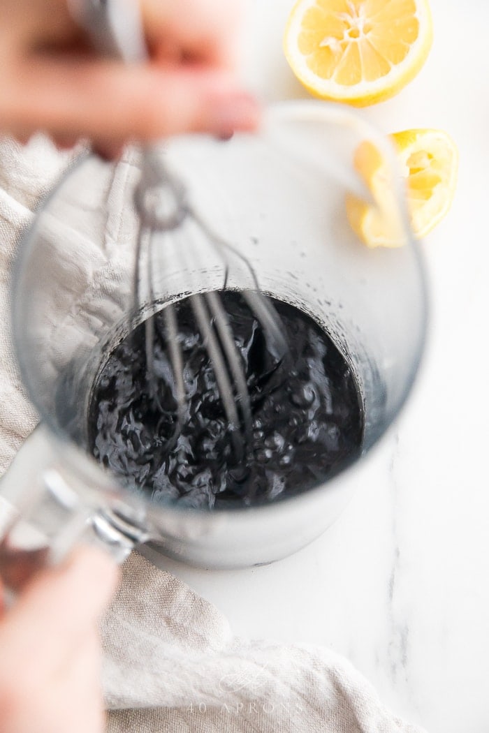 A whisk stirring charcoal lemonade ingredients in a pitcher