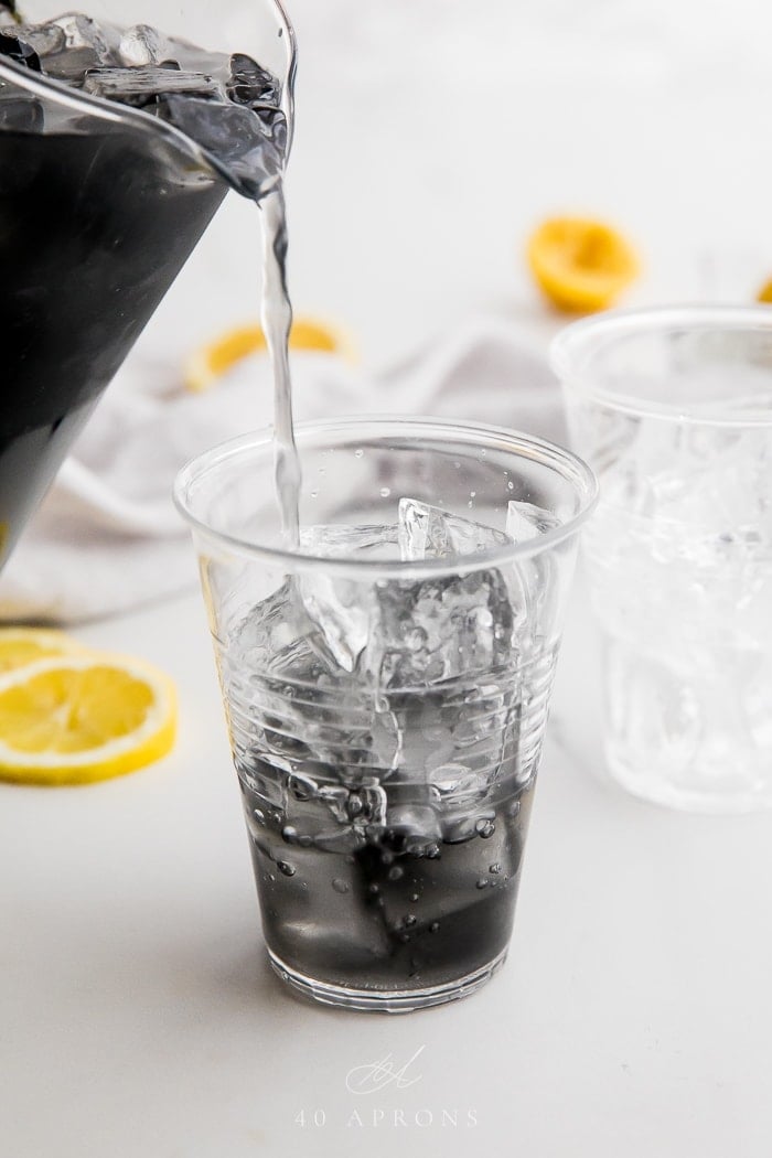 Pitcher pouring charcoal lemonade over ice