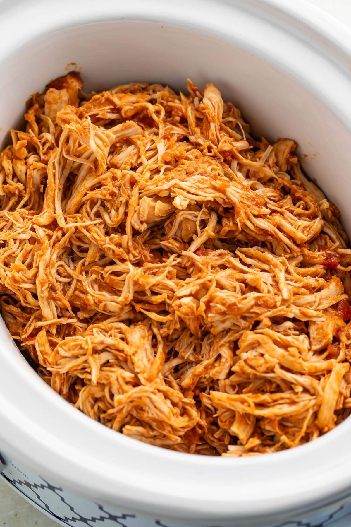 Shredded Mexican chicken in a white slow cooker on a kitchen counter.