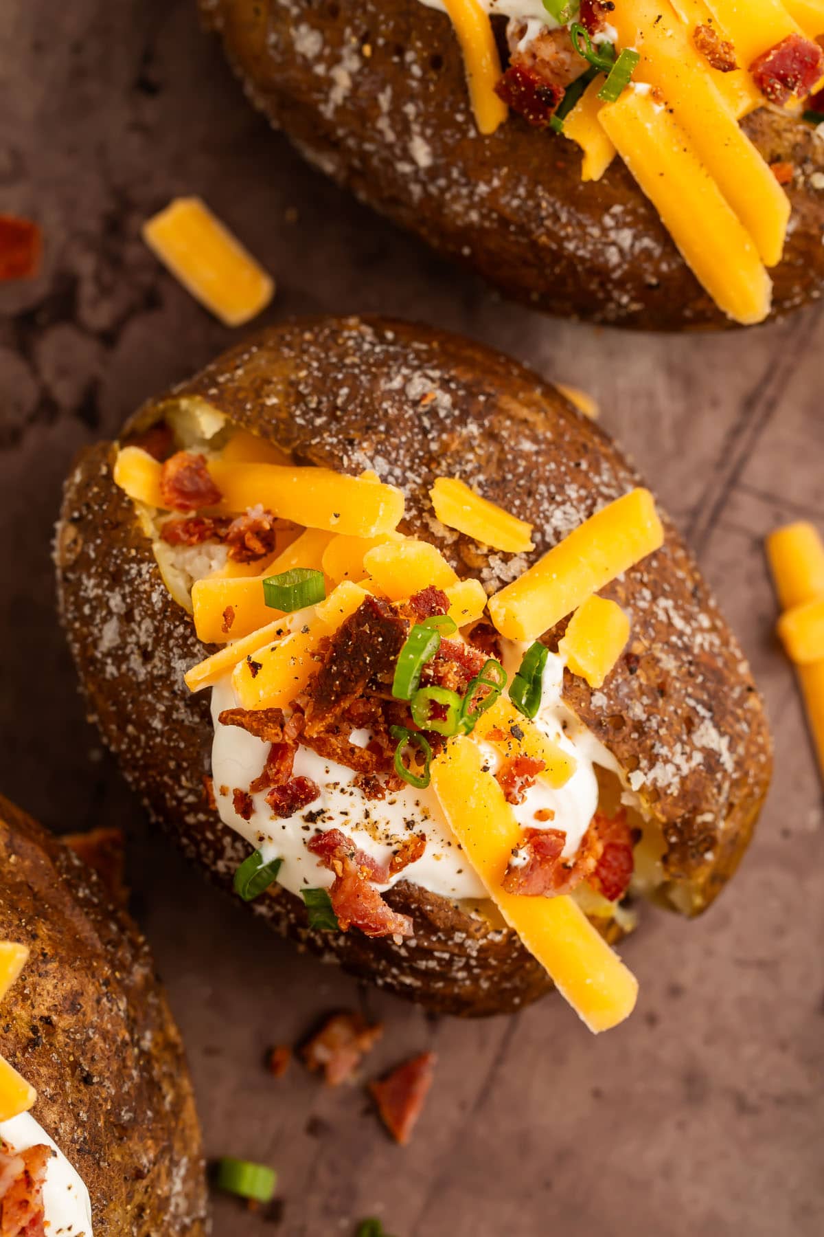 Baked potatoes, cooked on a grill, split open down the center then topped with a dollop of sour cream, shredded cheddar cheese, green onions, and crumbled bacon.