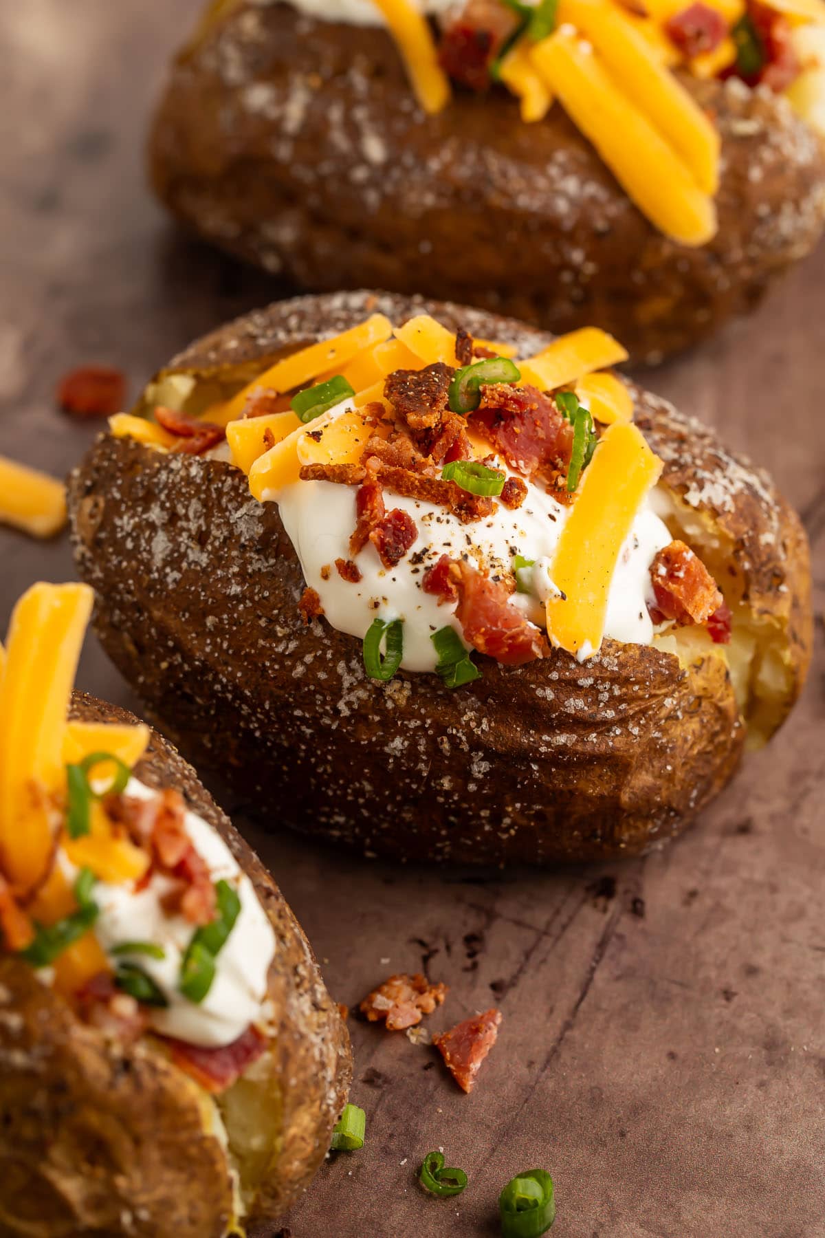 Baked potatoes, cooked on a grill, split open down the center then topped with a dollop of sour cream, shredded cheddar cheese, green onions, and crumbled bacon.