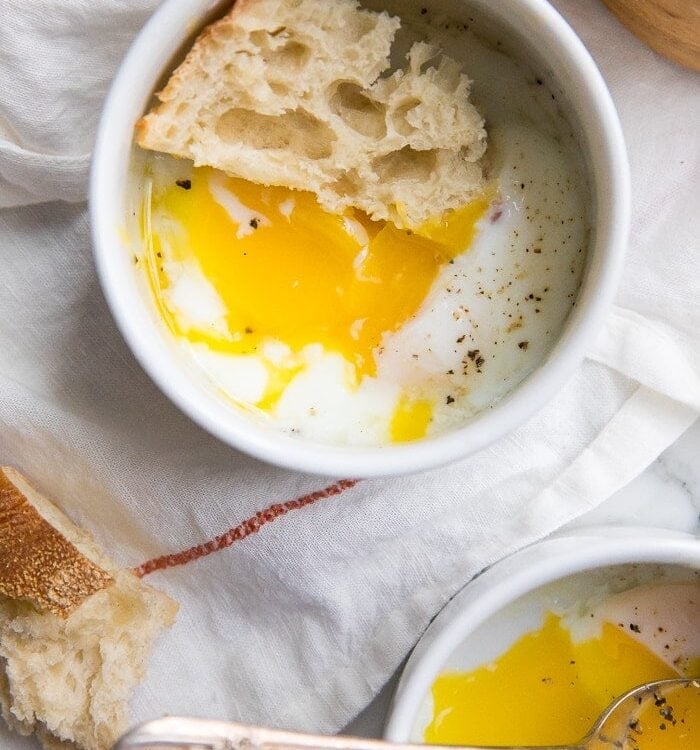 Sous vide eggs in small white bowls with crusty bread on top