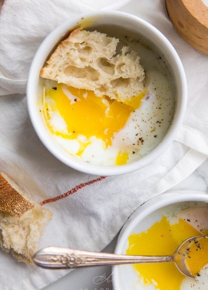 Sous vide eggs in small white bowls with crusty bread on top