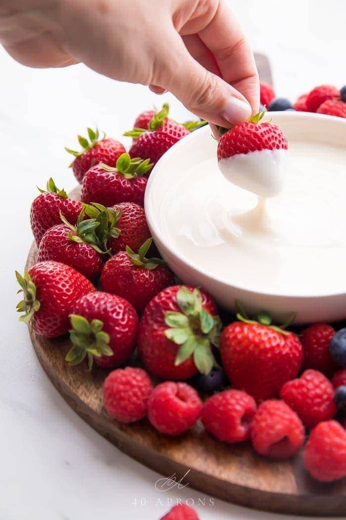 A bowl of yogurt fruit dip with a strawberry dipping in it