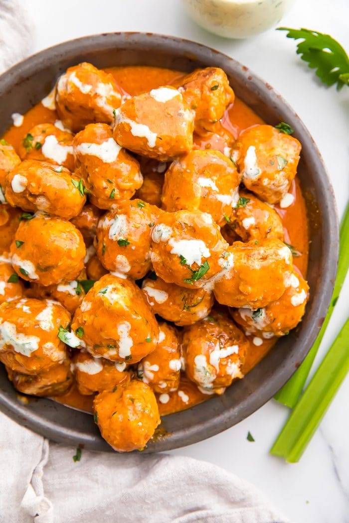Buffalo Chicken Meatballs served in a bowl with ranch dressing and fresh herbs