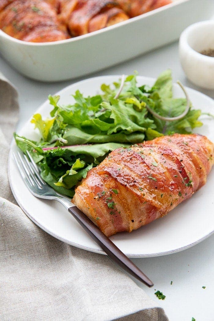 Bacon wrapped chicken served on a plate with a salad and a fork