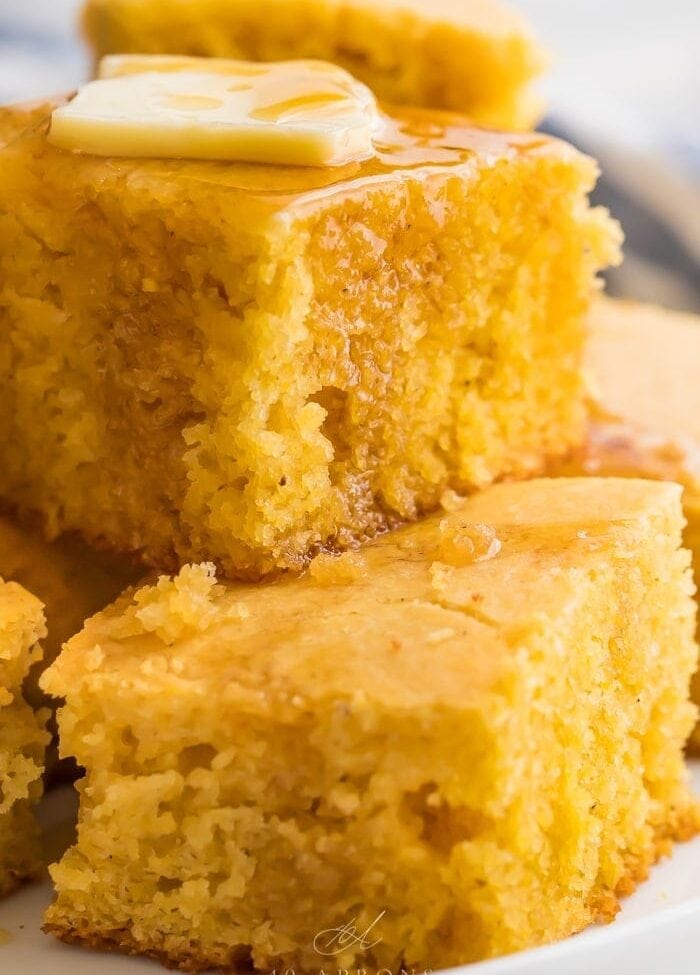 Gluten free cornbread stacked on a white plate with butter and honey