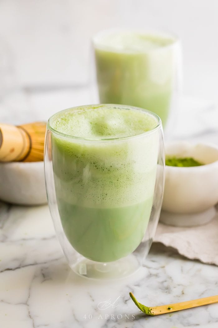 Two matcha lattes in glasses on a marble work surface