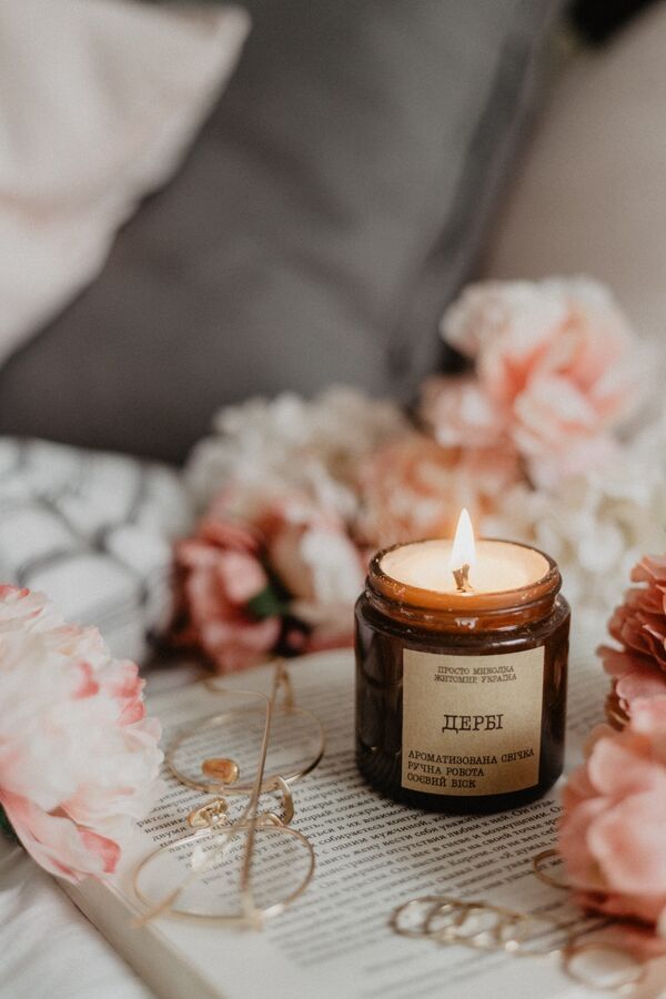 a scented candle on an opened book with golden glasses on the side and flowers in the background