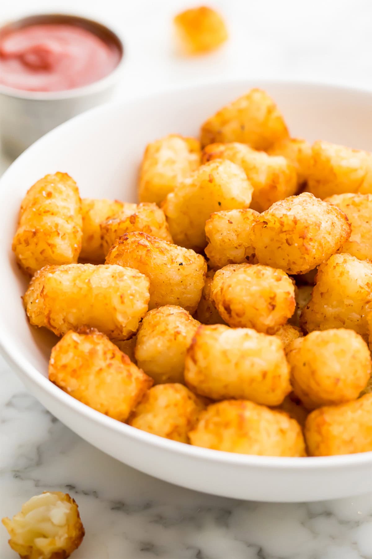 A side-view of a white bowl holding crispy air fryer tater tots.