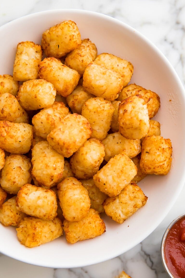 Overhead photo of a bowl of air fryer tater tots next to a small ramekin of ketchup.