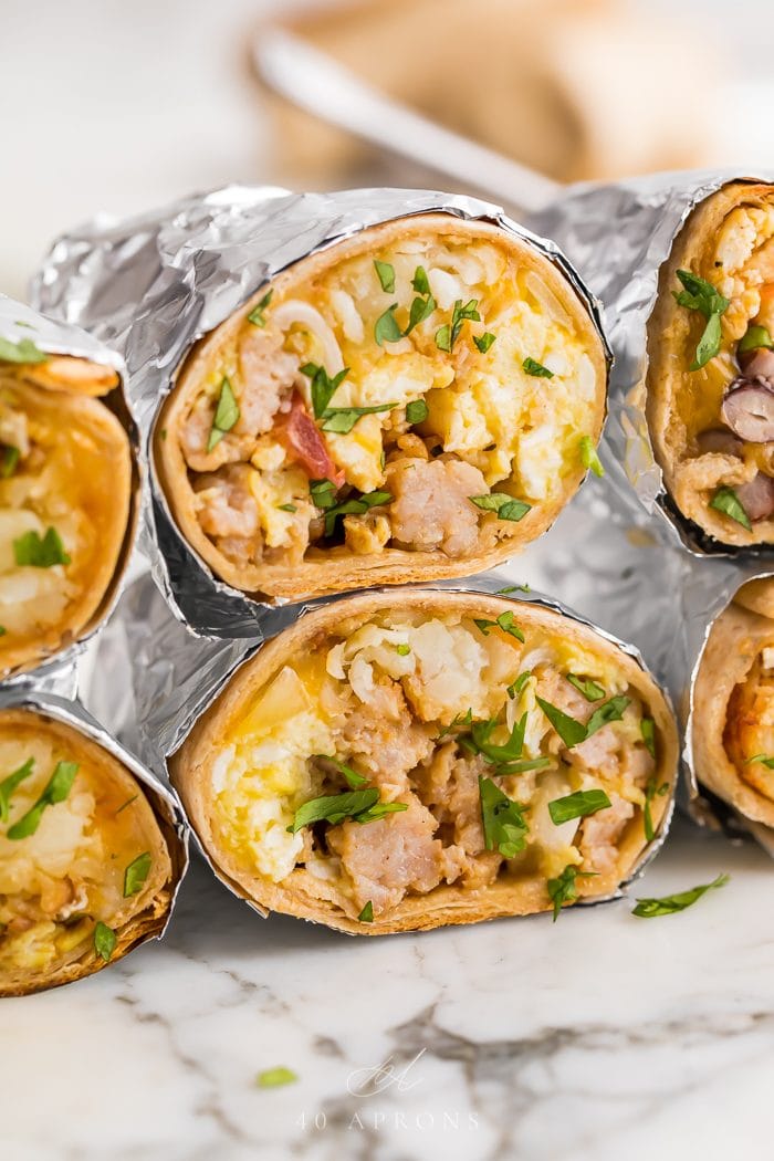 stacked healthy freezer breakfast burritos wrapped in aluminum foil