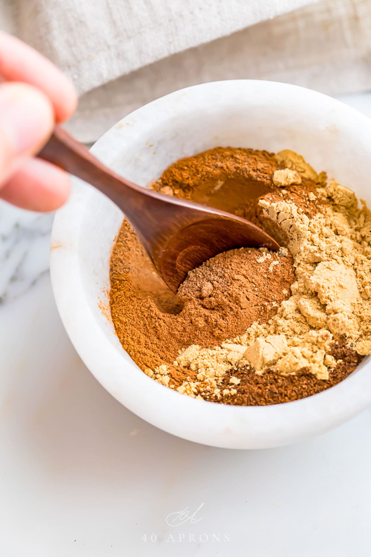 Spices being stirred together with a wooden spoon in a small marble bowl to make a homemade pumpkin pie spice blend.