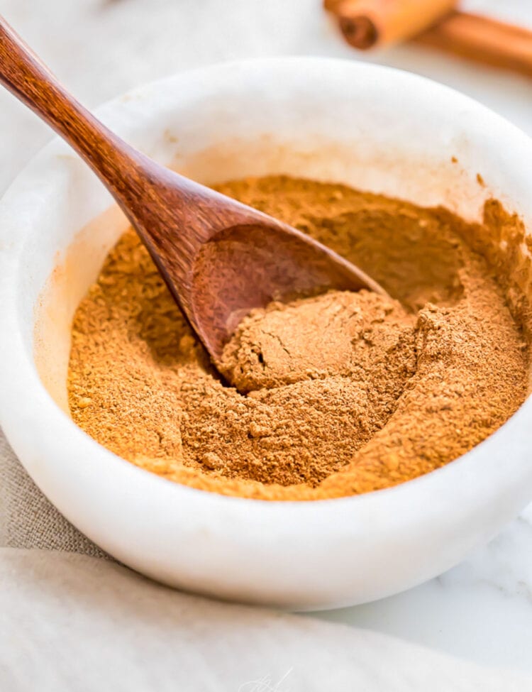 Homemade pumpkin pie spice blend in a small marble bowl with a small wooden spoon.