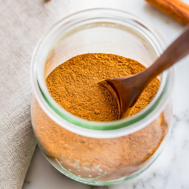 Homemade pumpkin pie spice blend in a glass jar with a wooden spoon.