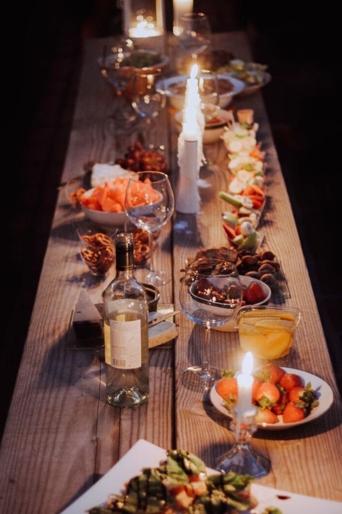 a long rustic wooden dinner table laid out for a hygge dinner party with lots of candles and fall-themed dishes