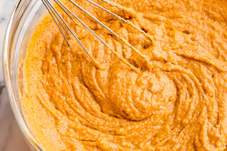 Prepared batter for pumpkin muffins in a large glass mixing bowl with a silver whisk.