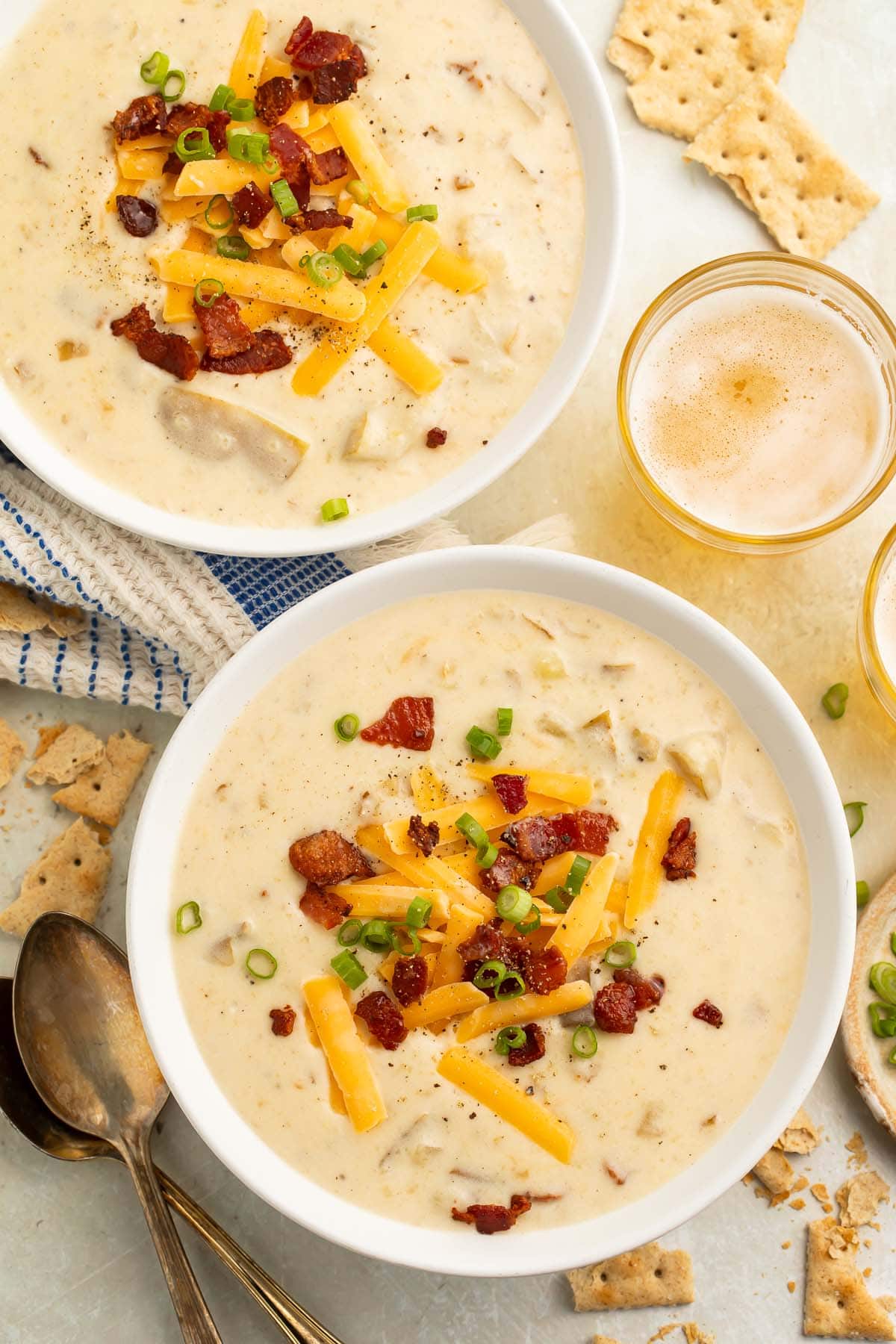 A large white bowl of creamy Crockpot potato soup topped with pieces of bacon and large shreds of cheddar cheese.