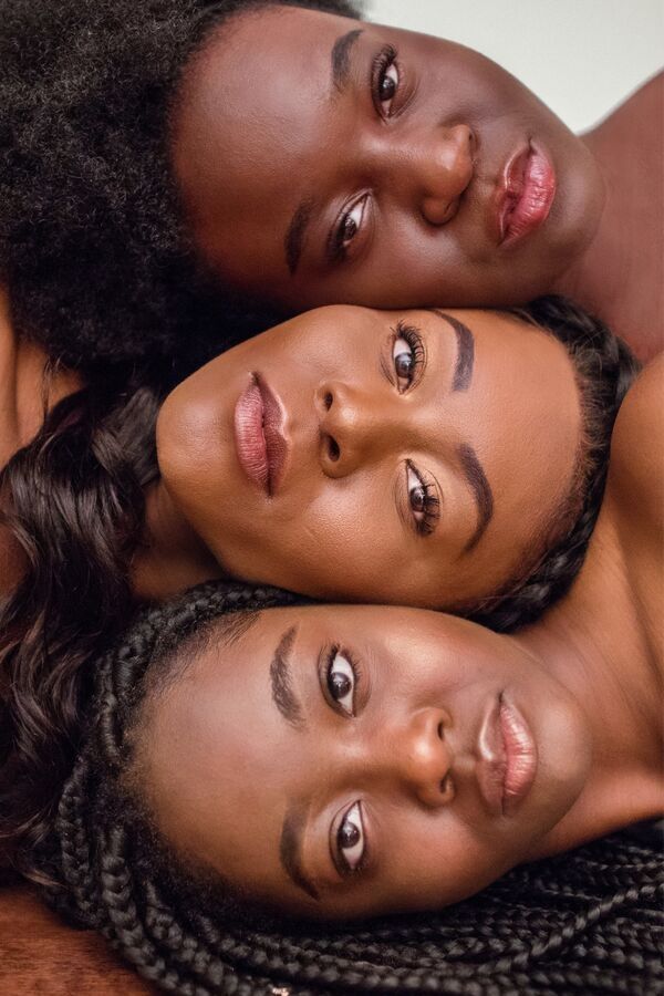 three dark skinned women with very clear skin lying next to each other in a line with their faces facing upwards