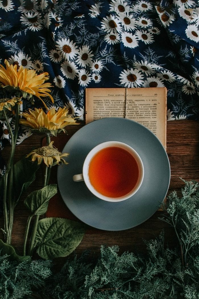 a cup of herbal reishi mushroom tea next to an antique book and some herbs and flowers