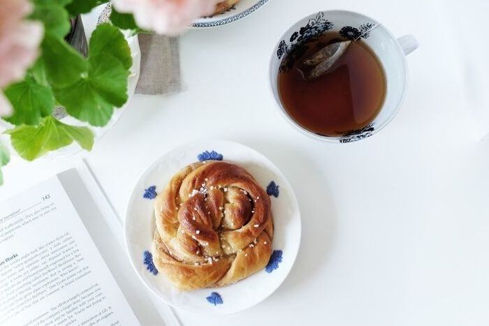 a cinnamon roll between a mug of tea and a book