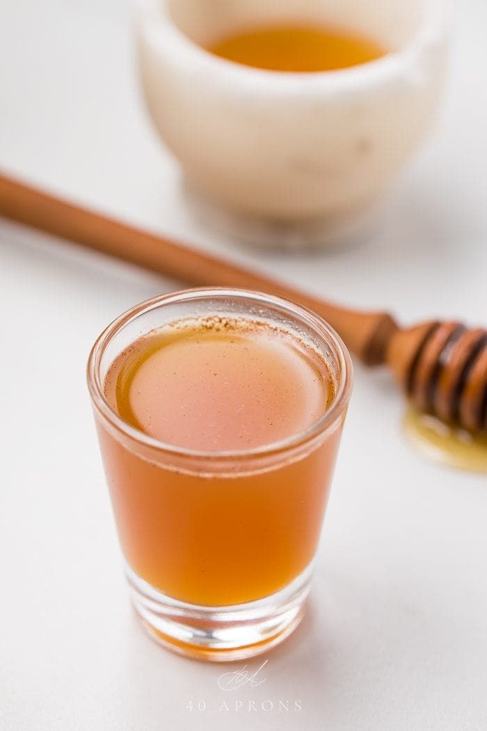 A apple cider vinegar shot in front of a honey dipper