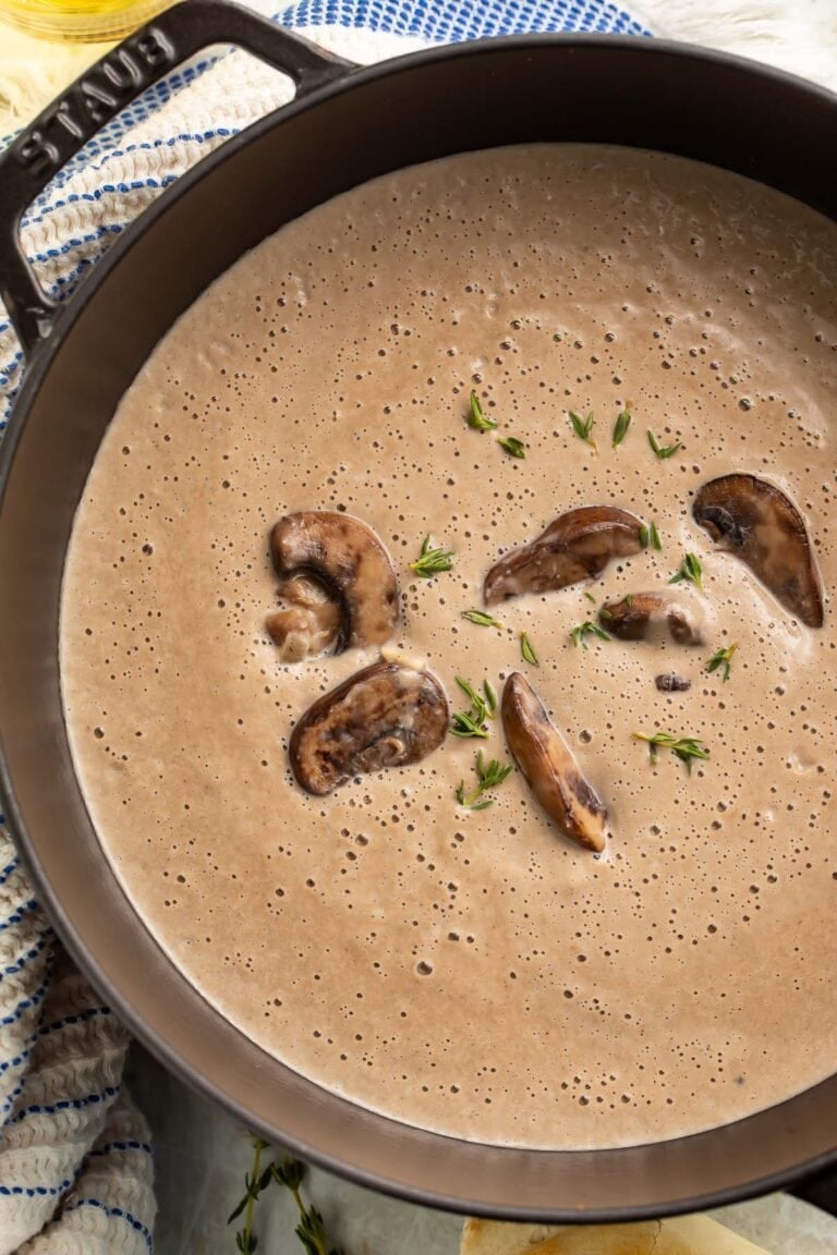 Overhead view of rich, thick, greyish-brown cream of mushroom soup in a large round black pot.