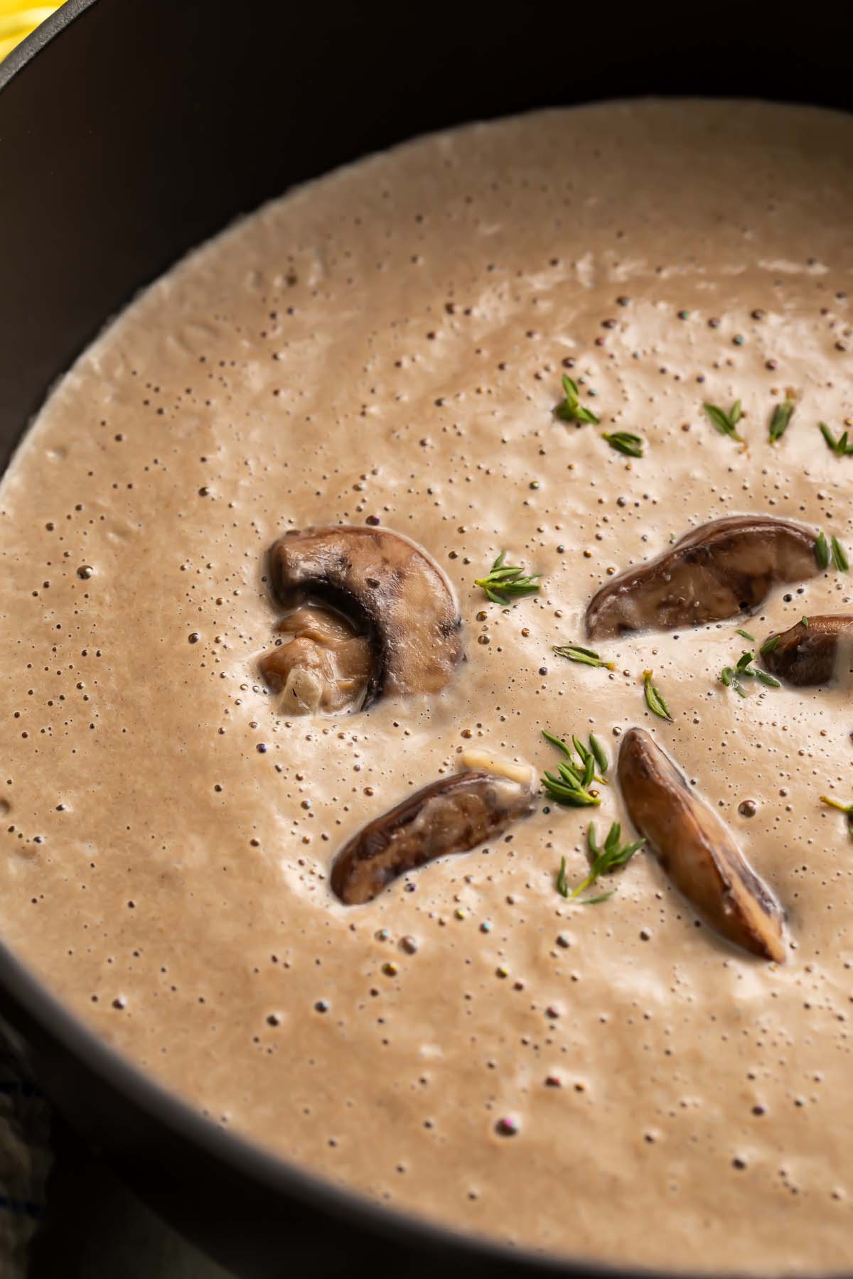 Overhead view of rich, thick, greyish-brown cream of mushroom soup in a large round black pot.