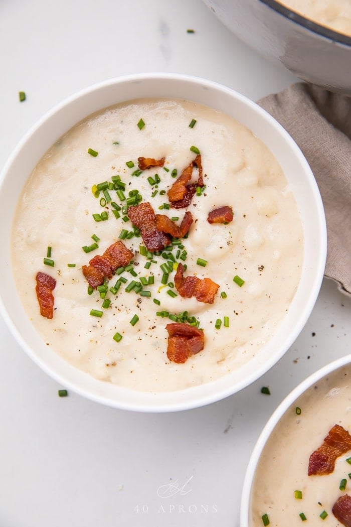 Bowl of potato soup topped with bacon bits and fresh chives